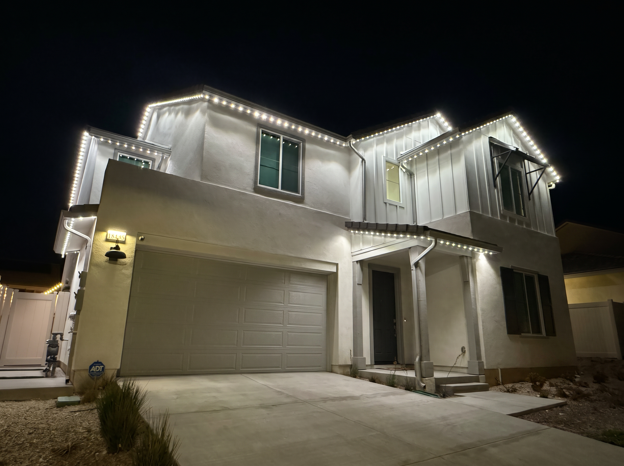 Two-story home outlined with permanent white LED roofline lighting at night